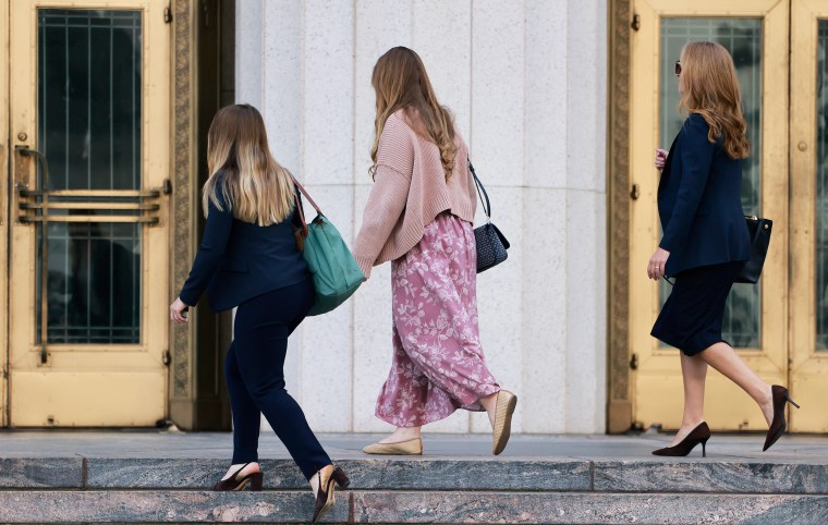 Three women are seen in profile view as they ascend the stone steps to a courthouse.